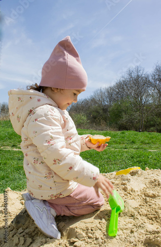 Little girl in the sandbox with shovels and a bucket on the playground. Child outdoors in summer. Summer fun. Summer sunny day in the sandbox.