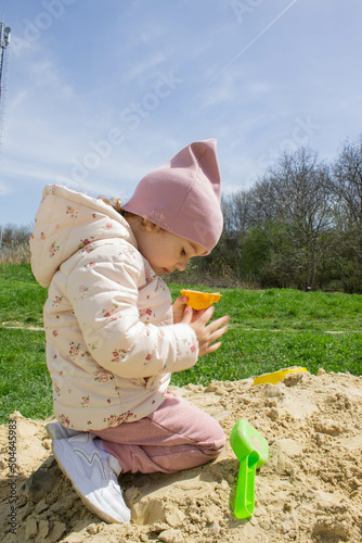 Little girl in the sandbox with shovels and a bucket on the playground. Child outdoors in summer. Summer fun. Summer sunny day in the sandbox.