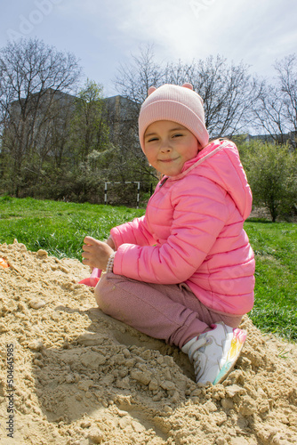 Little girl in the sandbox with shovels and a bucket on the playground. Child outdoors in summer. Summer fun. Summer sunny day in the sandbox.