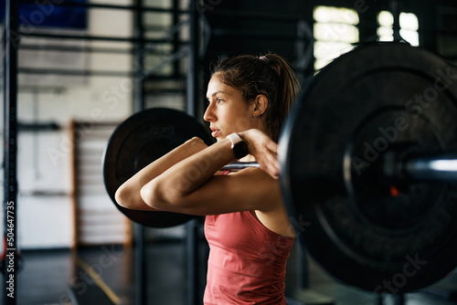 Athletic woman having strength training with barbell while working out in gym.