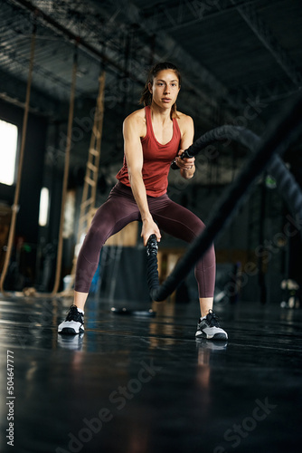 Young athletic woman using battle ropes during cross training at gym.