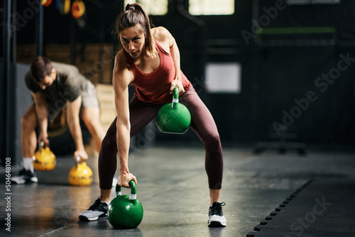 Female athlete having strength training with kettlebells in health club.