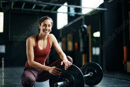 Young happy sportswoman during weight training in gym looking at camera.