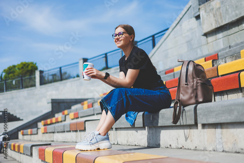Woman sits on steps and holds a disposable cup of coffee.