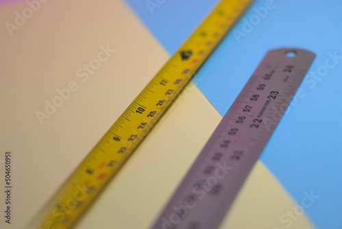 Yellow measuring tape and stainless steel ruler on blue and yellow surface
