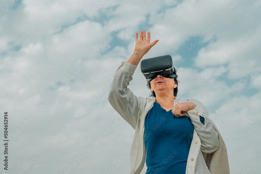 an adult woman against a blue sky with white clouds in VR virtual reality glasses on her eyes, covered with a blanket. older generation technologies an adult woman against a blue sky with white clouds in VR virtual reality glasses on her eyes, covered with a blanket. older generation technologies