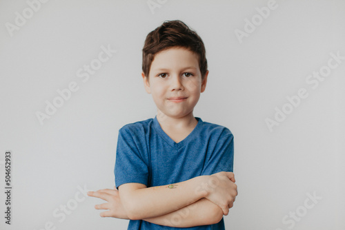 A preschool boy in a blue T-shirt on a light background shows a thumbs up