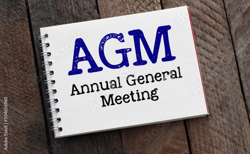 AGM Annual General Meeting words in notebook and wooden background. photo