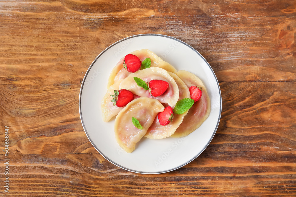 Plate with tasty strawberry dumplings on wooden background