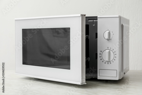 Microwave oven with opened door on table against light background
