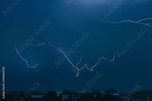 Lightning in sky over city. Bright flashes on dark night. Thunderclouds and electricity discharges in atmosphere.