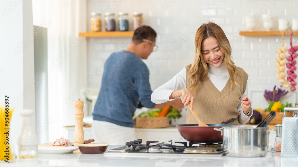 Asian people friends enjoy cooking pasta in cooking pan with talking together in the kitchen at home. Man and woman having dinner party meeting celebration eating food together on holiday vacation