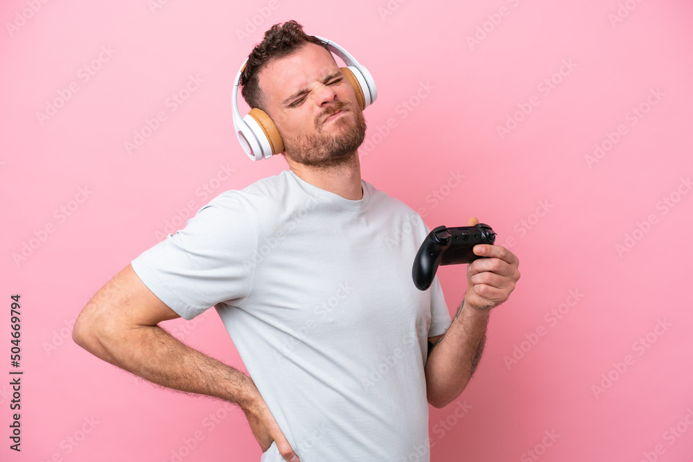 Young Brazilian man playing with video game controller isolated on pink background suffering from backache for having made an effort