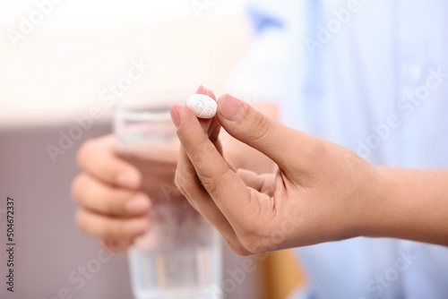Calcium supplement. Woman holding pill and glass of water on blurred background  closeup
