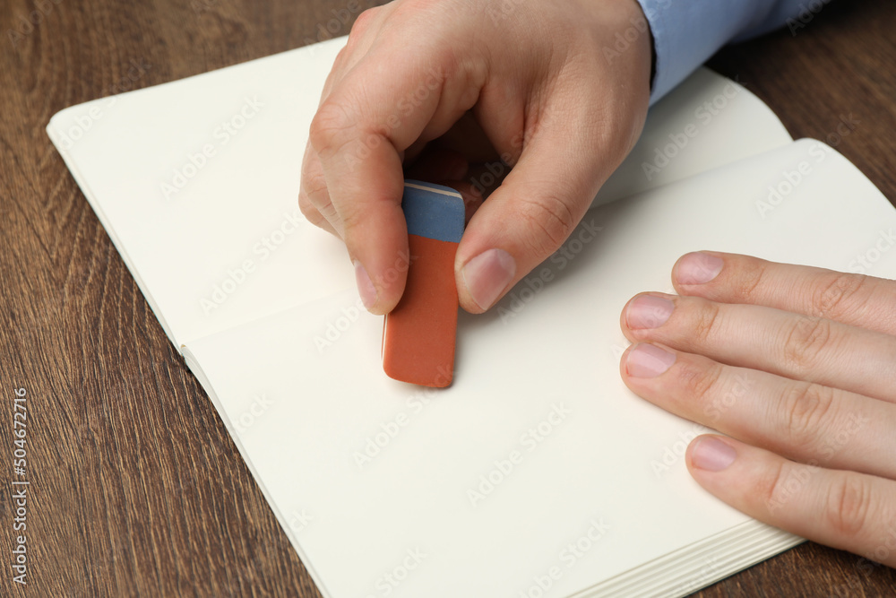 Man erasing something in notebook at wooden table, closeup Man erasing something in notebook at wooden table, closeup