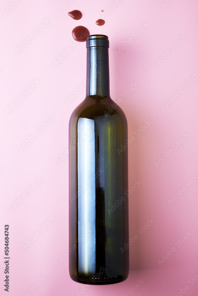 glass wine bottle and drops of red wine on a pink background glass wine bottle and drops of red wine on a pink background