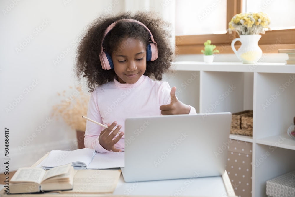 African girl in headphones looks at laptop show thumbs up during remote video call class with online tutor, express positive feedback, enjoy distancing homeschooling at home. Tech, education concept African girl in headphones looks at laptop show thumbs up during remote video call class with online tutor, express positive feedback, enjoy distancing homeschooling at home. Tech, education concept