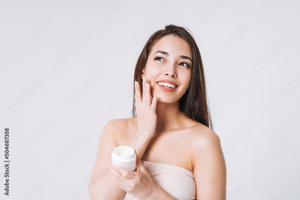 Beauty portrait of happy smiling asian woman with dark long hair put nourishing moisturizer cream on clean fresh skin face and hands on white background Beauty portrait of happy smiling asian woman with dark long hair put nourishing moisturizer cream on clean fresh skin face and hands on white background