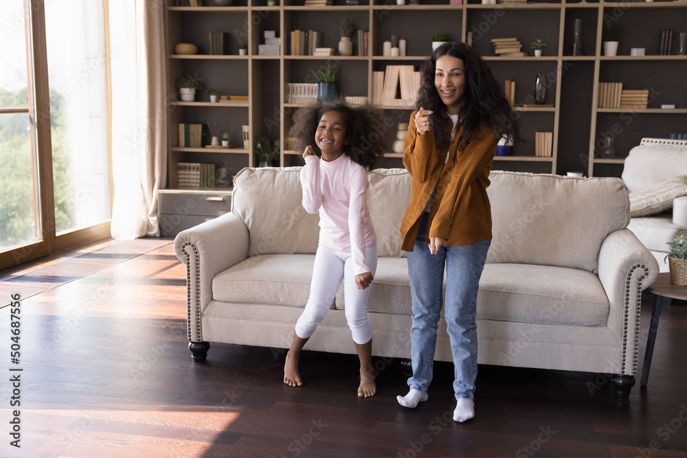 Cheerful African daughter and young mother dancing in cozy modern living room, have fun together at home enjoy carefree leisure and favourite music, listen song moving feel overjoyed. Pastime concept Cheerful African daughter and young mother dancing in cozy modern living room, have fun together at home enjoy carefree leisure and favourite music, listen song moving feel overjoyed. Pastime concept