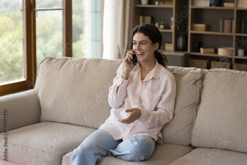 Happy young woman talk on smartphone relaxing on cozy sofa in living room, enjoy pleasant personal conversation, spend leisure alone at home. Mobile operator roaming usage, tech, communication concept