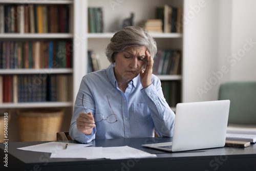 Exhausted frustrated mature business professional woman tired of work at laptop computer at office table workplace, feeling overworked, headache, migraine, suffering from bad weak vision, eyesight