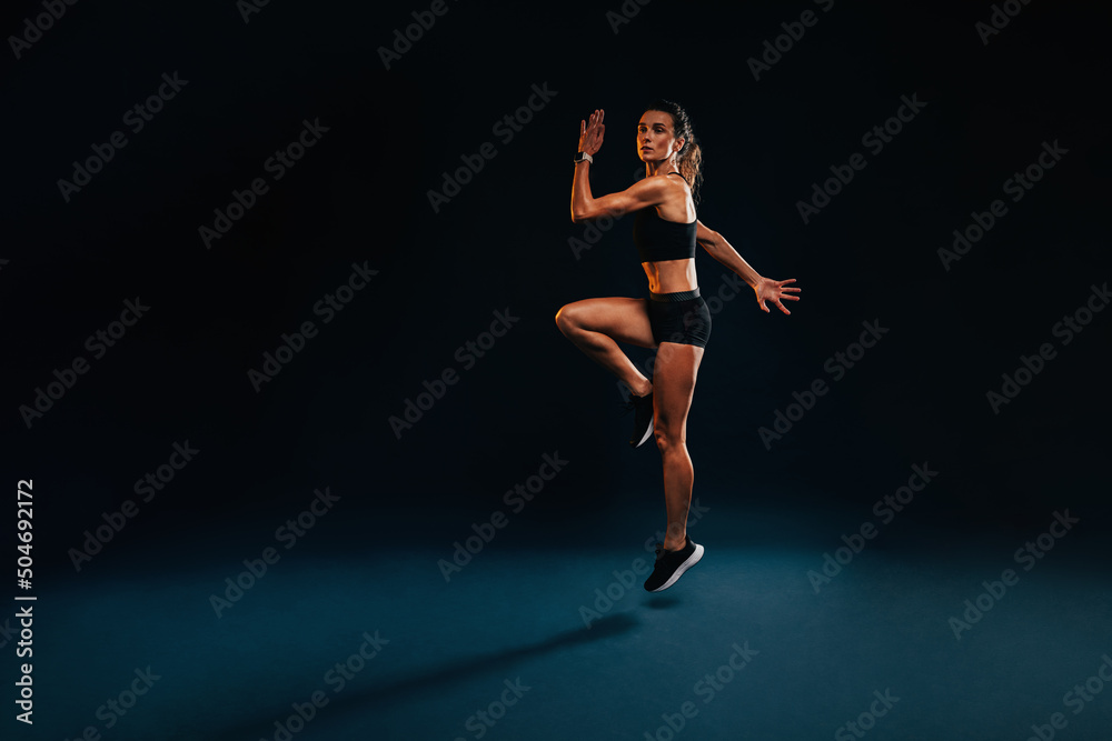 Obraz premium Female athlete jumping and stretching. Healthy woman exercising in studio warming up.