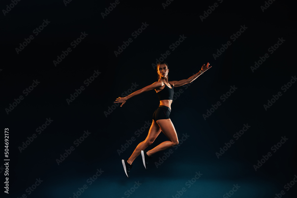 Slim woman working out on black background. Female athlete doing jumps in studio.