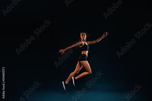 Slim woman working out on black background. Female athlete doing jumps in studio.