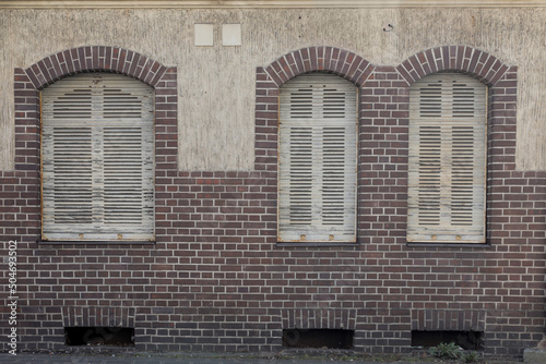 Old building with three closed windows, brick stone wall, and white shutter, no person