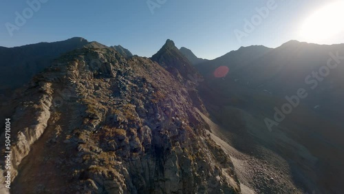 Aerial view mountain ridge structure with communication electricity tower sun light glare. FPV sports drone shot cliff rocky stones peak picturesque panorama nature landscape with technology pillar 4k photo