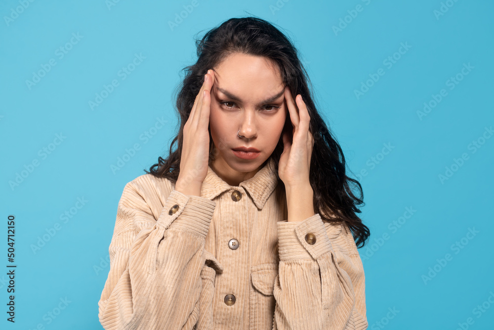 Sad tired young european lady brunette suffers from headache, presses hands to temples Sad tired young european lady brunette suffers from headache, presses hands to temples
