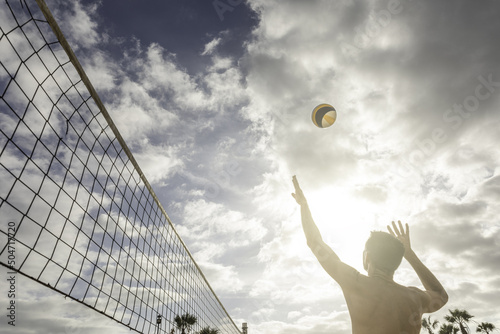 Man spiking a beach volleyball against the light. Summer vacation concept