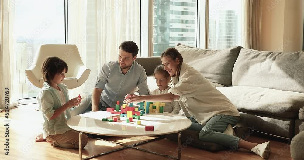 Wellbeing homeowner family spend weekend with cute preschool children, play wooden cubes seated on warm floor in sunny fashionable living room. Children development, leisure activity at home concept