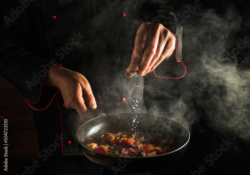 Fotografija Professional chef adds salt to a steaming hot pan