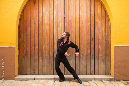 man dancing flamenco with black shirt and red roses  on a background of a wooden door  doing different postures while dancing. Flamenco dance concept cultural heritage of humanity. Feel de passion.