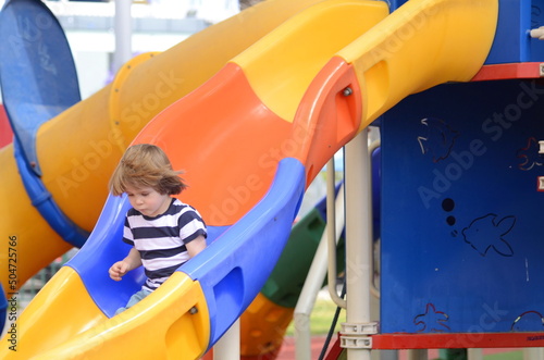 Child playing on outdoor playground. Kids play on kindergarten yard. Active kid on colorful slide. Funny toddler boy having fun on colorful slide 