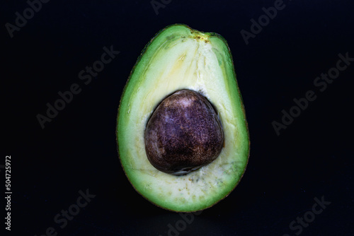 Hass avocado isolated in black background, decorated with wooden logs, macro shot using studio lighting
 photo