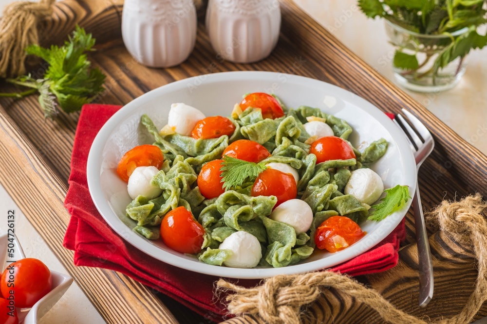 Homemade nettle tagliatelle with poached cherry tomatoes and mozzarella in a gray plate on a light concrete background. Italian food.