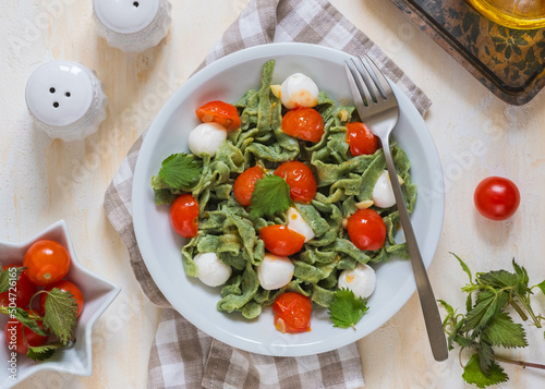Foto Homemade nettle tagliatelle with poached cherry tomatoes and mozzarella in a gray plate on a light concrete background