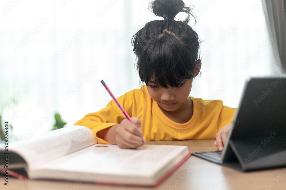 Kid holding pencil wring on paper, Child using digital tablet searching information on internet for his homework, Home schooling, E-learning online education Kid holding pencil wring on paper, Child using digital tablet searching information on internet for his homework, Home schooling, E-learning online education