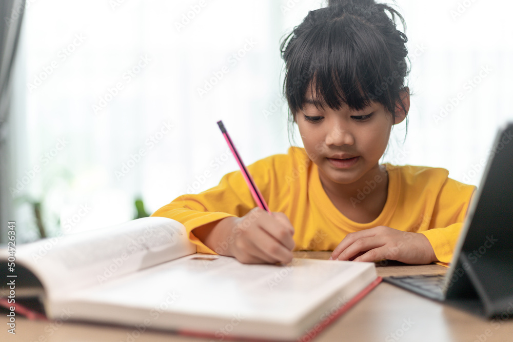 Kid holding pencil wring on paper, Child using digital tablet searching information on internet for his homework, Home schooling, E-learning online education Kid holding pencil wring on paper, Child using digital tablet searching information on internet for his homework, Home schooling, E-learning online education