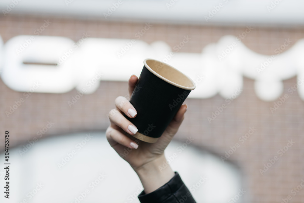 Girl holding a cardboard cup. Paper coffee cup in a woman hand on store background. Hot drink. Hand holding paper cup of coffee. Paper coffee cup.