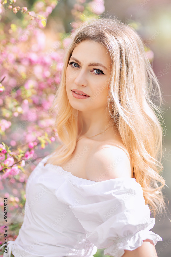 Blonde woman in white clothes next to a flowering tree or bush with pink flowers Blonde woman in white clothes next to a flowering tree or bush with pink flowers