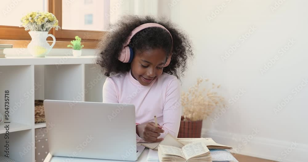 Little African girl in headphones sit at desk use laptop studying, e-learn school subject, learn topic take part in remote on-line class with tutor. Virtual lesson with teacher, homeschooling concept Little African girl in headphones sit at desk use laptop studying, e-learn school subject, learn topic take part in remote on-line class with tutor. Virtual lesson with teacher, homeschooling concept