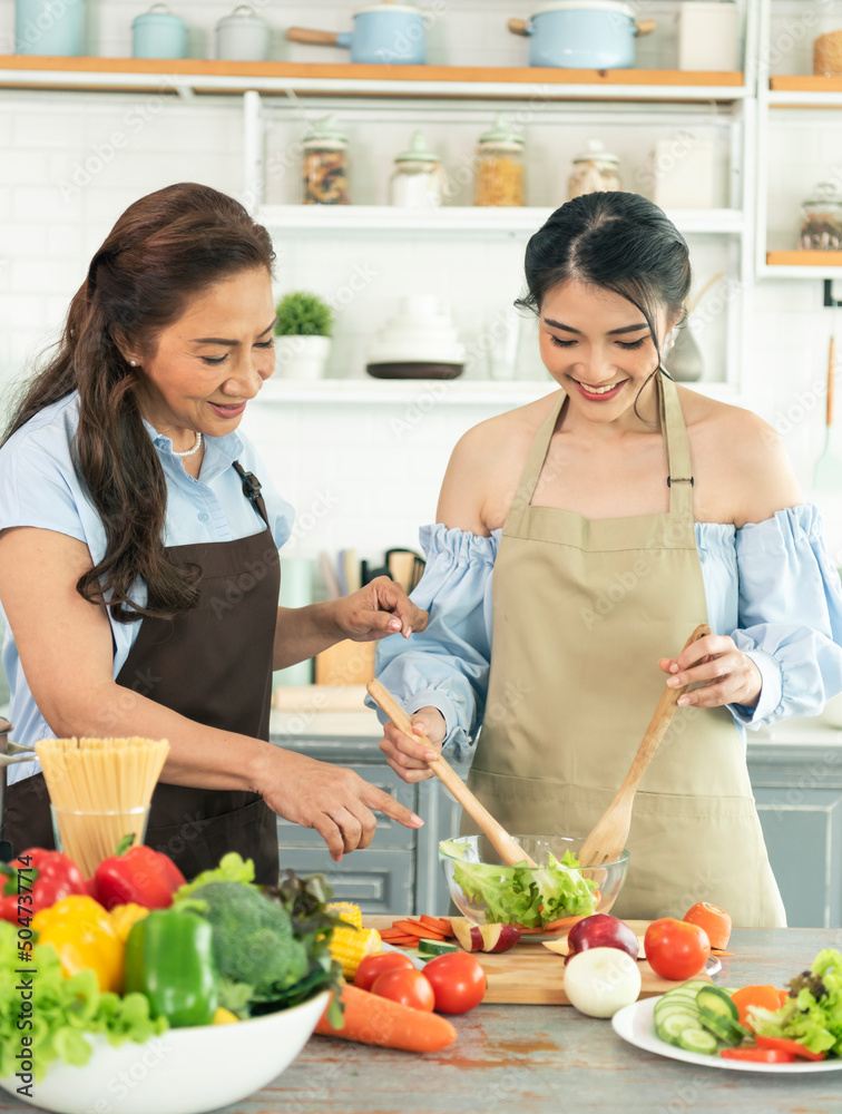 Happy Asian family mother teaching daughter to making salad in kitchen at home. Enjoy family activity together.