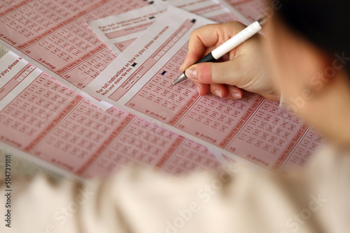 Filling out a lottery ticket. A young woman plays the lottery and dreams of winning the jackpot. Female hand marking number on red lottery ticket photo