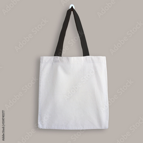 White blank cotton eco tote bag with black straps, design mockup. Shopping bag hanging on wall
