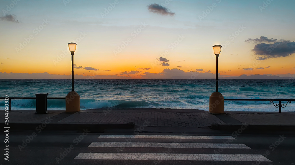 The beach of Rhodes Greece at sunset and two street lights and crosswalk lines