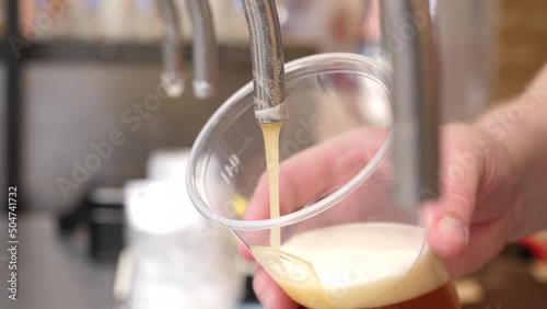 Closeup seller pouring a beer with white foam in plastic disposable cup on a street food fair festival on city public event