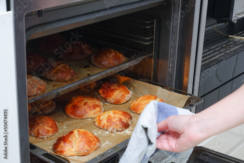 Woman opens the oven where cookies are baked and admiring delicious croissants o Fototapeta